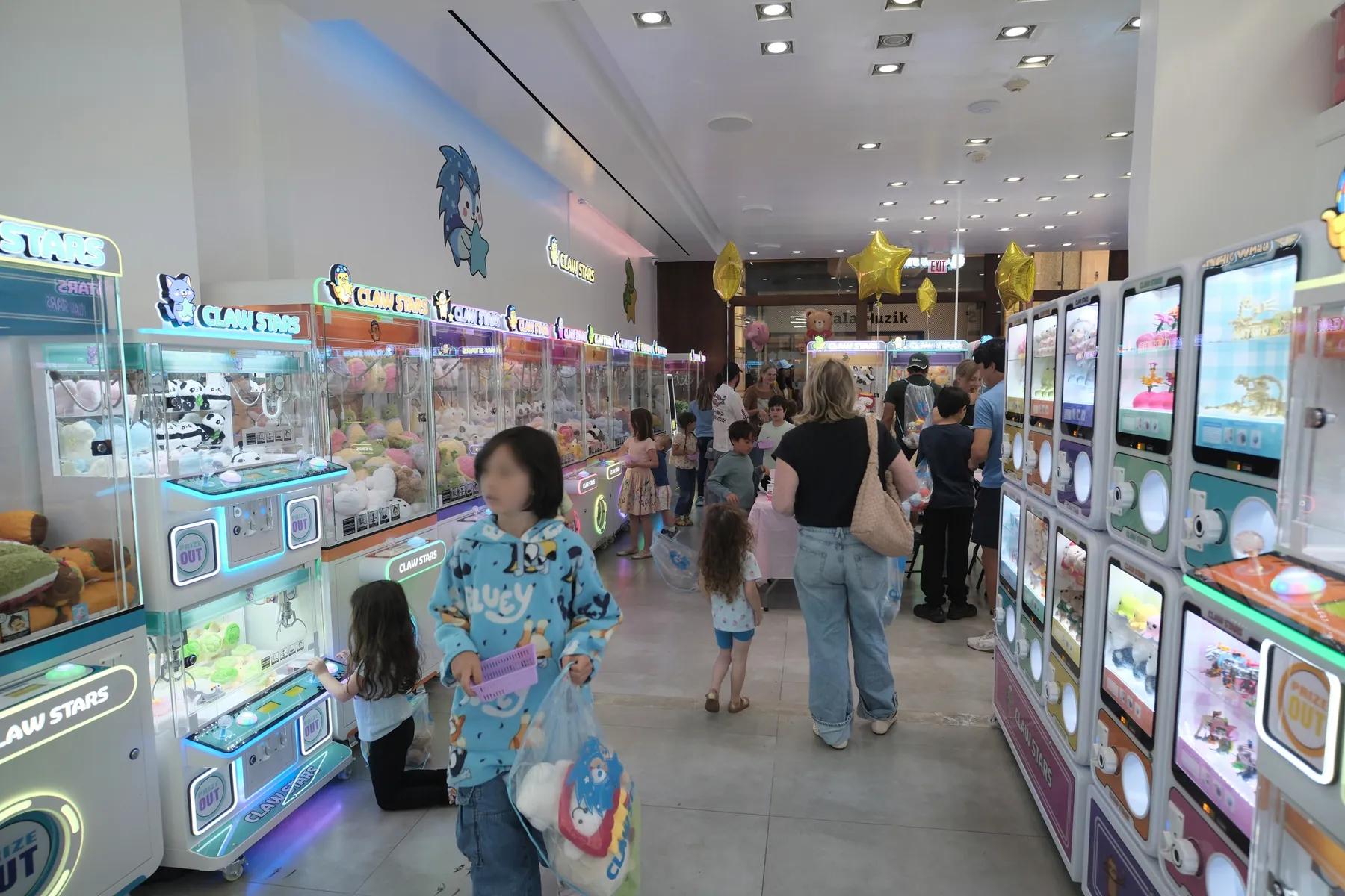 A busy Saturday on the Claw Stars floor, families playing along a long aisle of lit claw machines