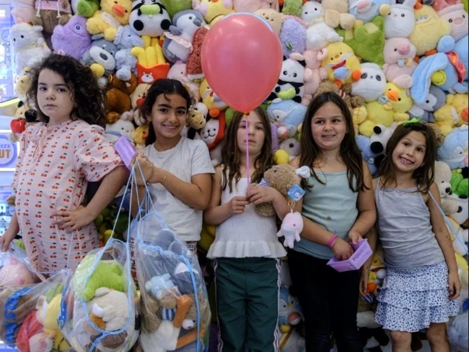 Five girls at a birthday party holding a bag of plushies in front of the Claw Stars prize wall