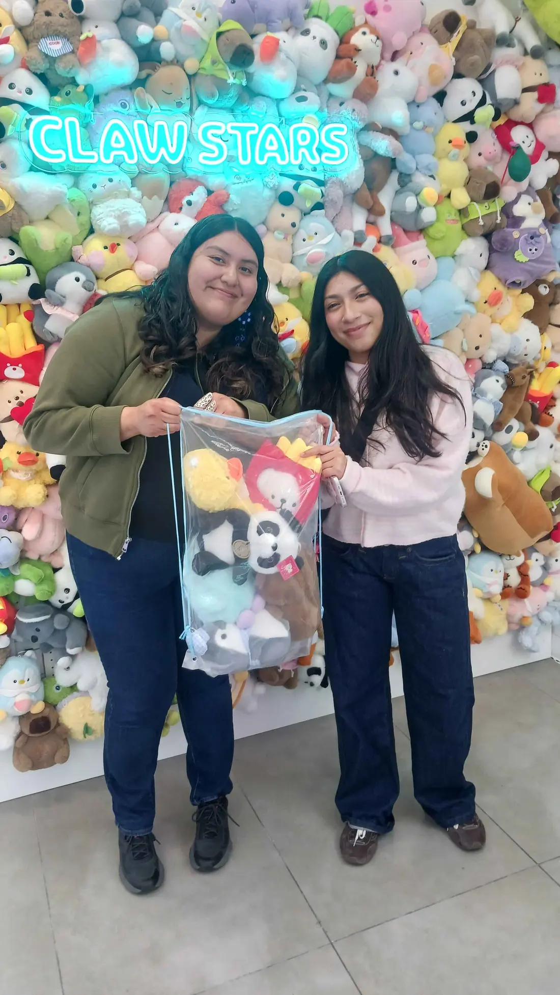 Two friends holding up a clear bag stuffed with plushies they won