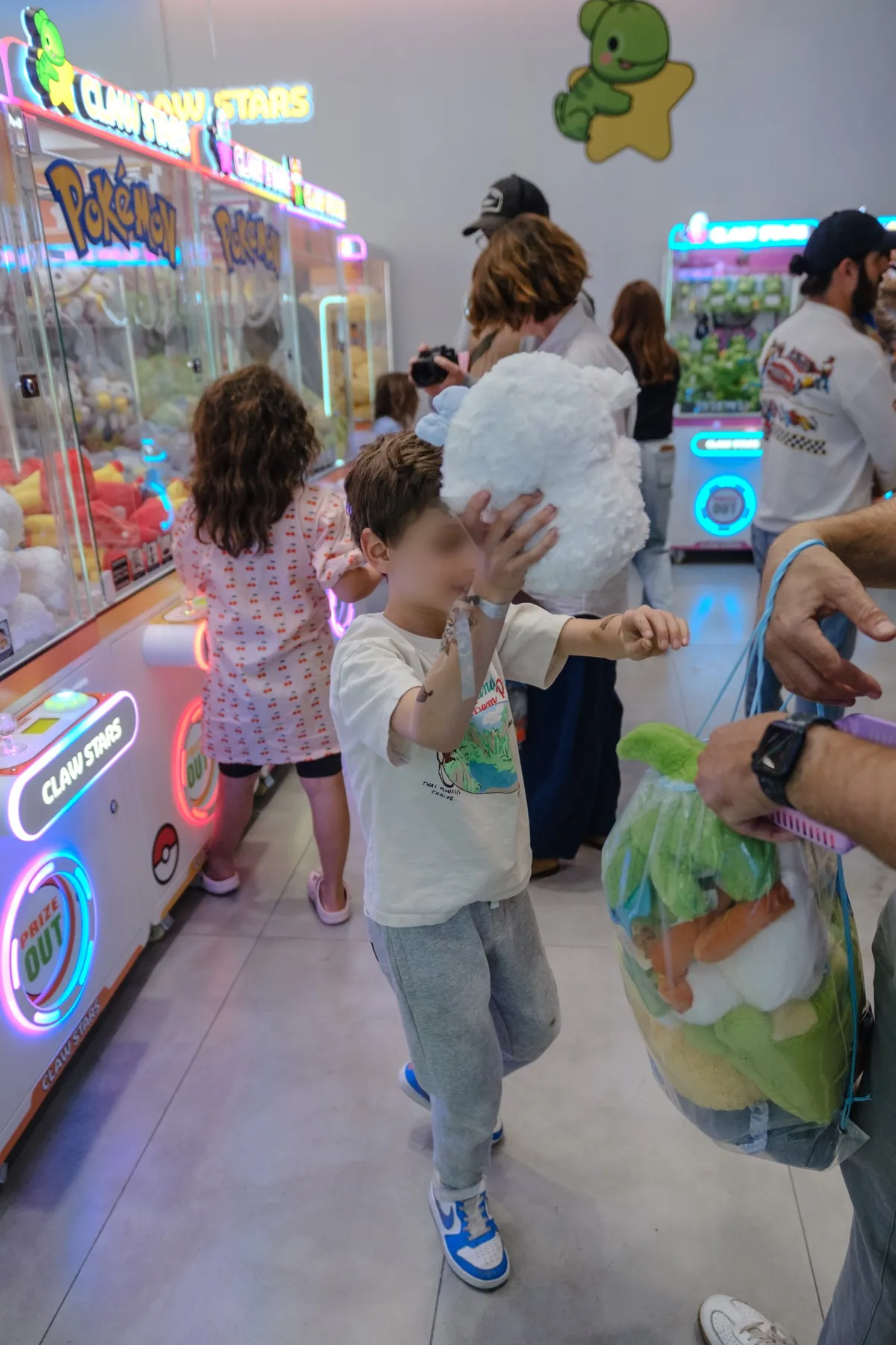 A small boy reaching up for the oversized white plushie an attendant is handing him